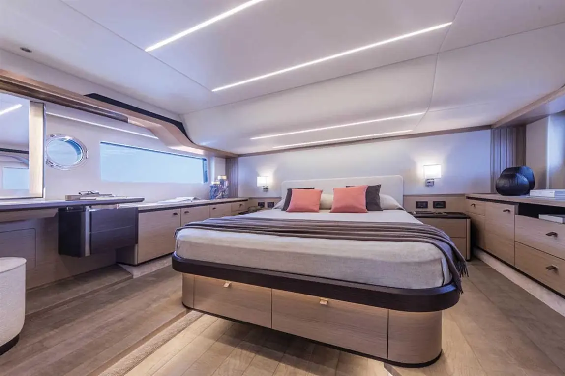 Luxurious yacht interior featuring a double bed with pink cushions, modern lighting, and elegant wooden furniture.